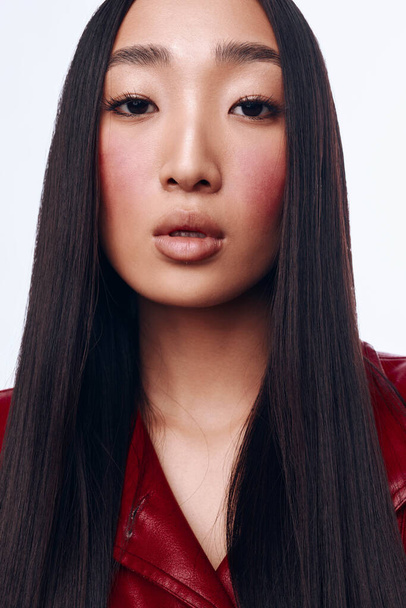 スタイリッシュな都市設定でカメラのためにポーズする長い黒髪と赤いジャケットを持つ若いアジアの女性 - 写真・画像