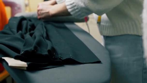 close-up em uma oficina de costura uma costureira mede em um tecido preto onde fixar - Filmagem, Vídeo