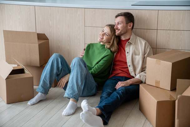 Šťastný pár muž žena objímající sní o bydlení v novém bytě sedí na podlaze v kuchyni doma. Přemístění, stěhování do bytu, rodinná hypotéka. Manželé si užívají životní změny odpočinku. - Fotografie, Obrázek