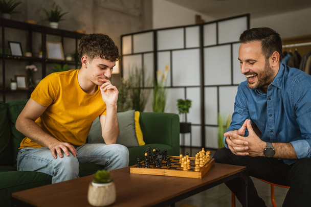 mladí a dospělí kavkazští muži přátelé, bratranci nebo bratři hrají spolu doma šachy - Fotografie, Obrázek