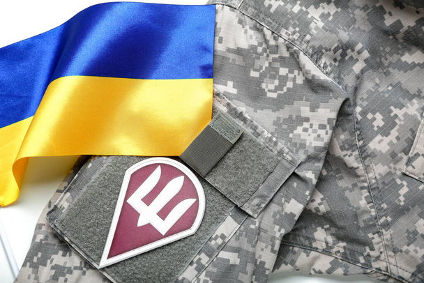 Insignia con tridente en uniforme militar y bandera de Ucrania, primer plano - Foto, imagen