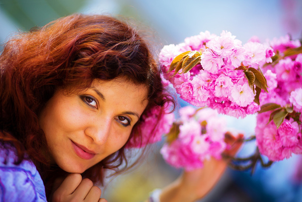 Młoda kobieta wąchająca piękny kwiat sakury, purpurowe kwiaty. Wiosenna magia - Zdjęcie, obraz