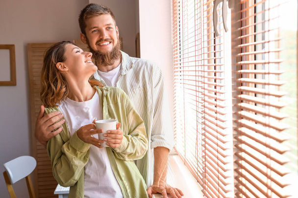 Couple heureux amoureux avec tasse de café près de la fenêtre à la maison - Photo, image