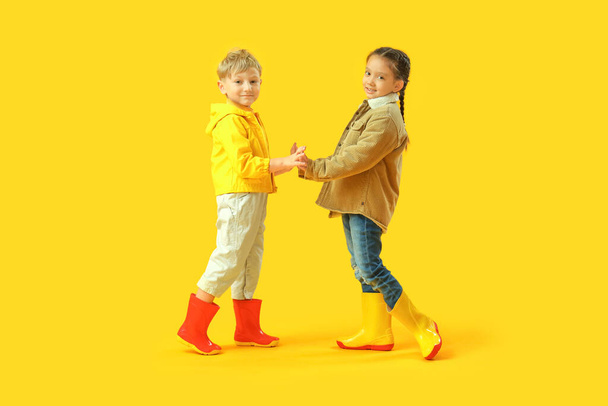 Małe dzieci w gumowych butach trzymające się za ręce na żółtym tle - Zdjęcie, obraz