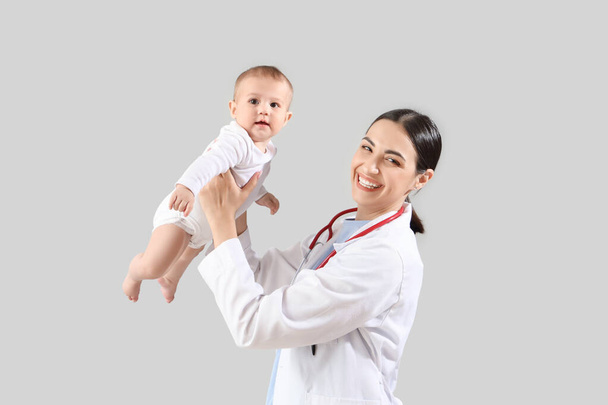 Female pediatrician with little baby on light background - Fotoğraf, Görsel