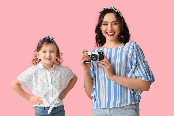 Όμορφη γυναίκα με φωτογραφική μηχανή και την κόρη της σε ροζ φόντο - Φωτογραφία, εικόνα