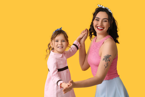 Beautiful pin-up woman and her daughter on yellow background - Fotografie, Obrázek