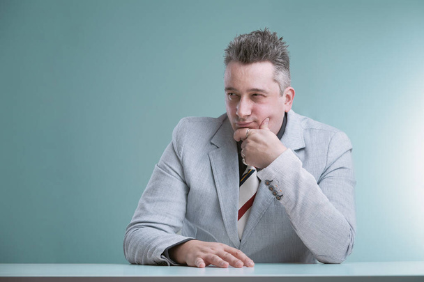 Pensive professional in grey suit with spiked hair appears contemplative, hand on chin, reflecting quietly - Photo, Image