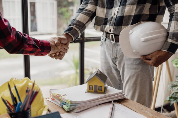 Architect and construction engineer holding hands while working for teamwork and cooperation concept after completing an agreement at construction site, office, close-up image - Фото, изображение