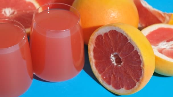 Grapefruitová šťáva v brýlích mezi čerstvými grapefruity na modrém pozadí. - Záběry, video