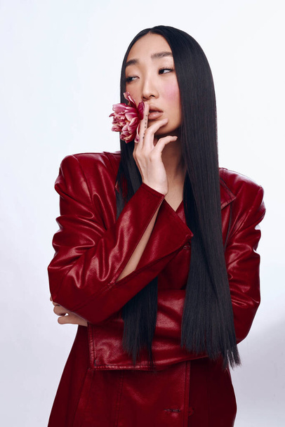 Elegante donna con lunghi capelli neri indossando giacca di pelle rossa e tenendo il fiore in mano - Foto, immagini