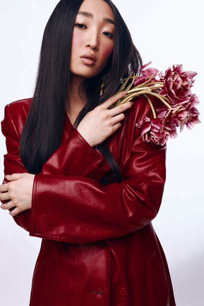 Stylish Asian Woman in Red Leather Jacket Holding a Bouquet of Flowers on Urban Background - Photo, Image