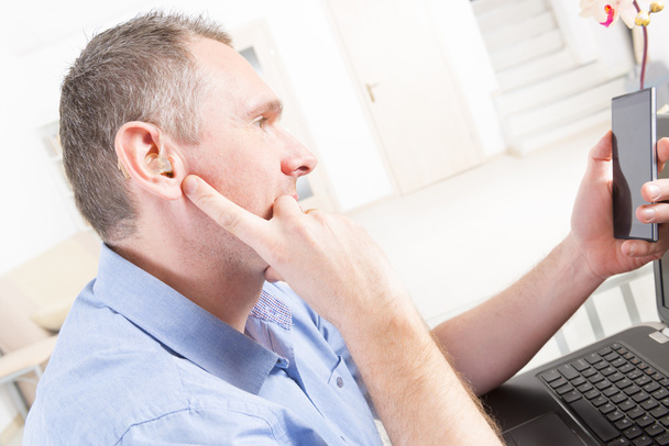 Άνθρωπος με προβλήματα ακοής που εργάζονται με φορητό υπολογιστή και κινητό τηλέφωνο - Φωτογραφία, εικόνα