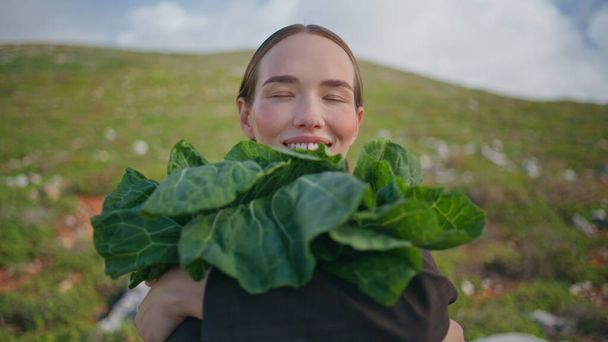 Frau hält Blattgemüse in Großaufnahme auf einem Feld. Glückliches Mädchen posiert mit Kohl und genießt die Ernte. Lächelnder Gärtner mit grünem, frischem Grünkohl zeigt Bio-Ernte. Veganes gesundes Ernährungskonzept - Foto, Bild