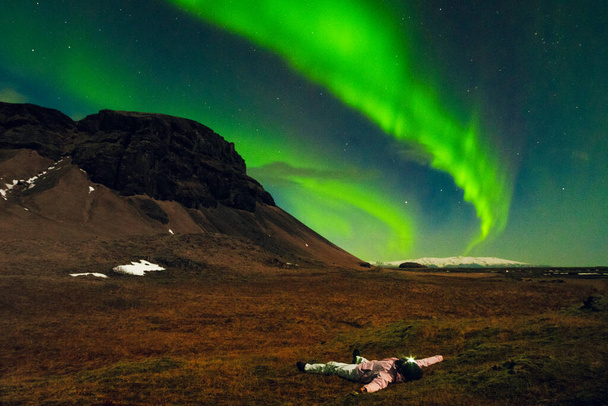 Une femme regarde les aurores boréales s'étendre sur un pré herbeux seul en Islande. Femme romantique en Islande nuit de printemps paysage Islande Voyage chasse concept aurores boréales - Photo, image