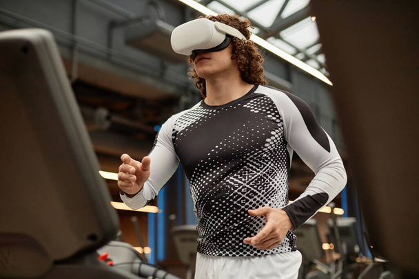 Taille omhoog portret van sportieve jongeman met VR-headset op loopband in de sportschool tijdens immersieve trainingssessie kopieerruimte - Foto, afbeelding