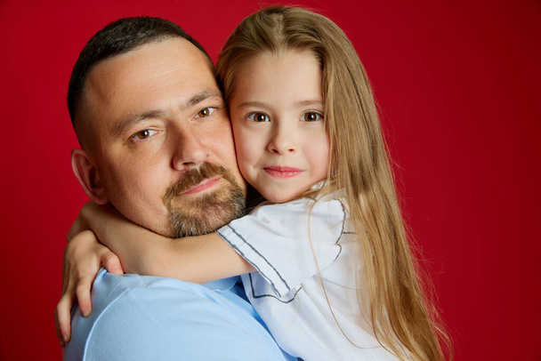Портрет молодого чоловіка тримає на руках свою улюблену маленьку дівчинку на фоні яскраво-червоної студії. Донька Дадса. Концепція Дня батька. Дитячий день, День сім'ї, батьківство. Реклама - Фото, зображення