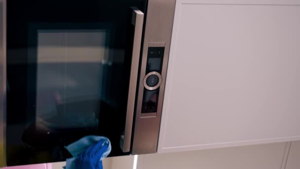 video verticale da vicino in un appartamento un pulitore in un grembiule giallo sta pulendo il forno con uno straccio blu - Filmati, video
