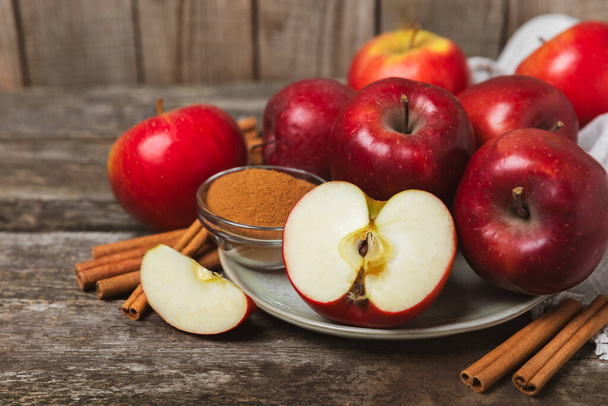 Apples with cinnamon on a textured wooden background. Fragrant red spiced apples with cinnamon sticks and star anise. Apple slices with spicy spices. Place for text. Copy space. Harvesting. Fruits.  - Photo, Image
