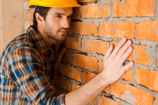 Man in hardhat touching brick wall - 写真・画像
