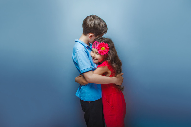 дівчина-підліток обіймає хлопчика-підлітка на сірому фоні
 - Фото, зображення