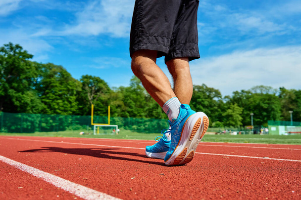 Athlete wearing blue Asics Gel-Nimbus 25 running shoes on red stadium track during training. Sportsman legs in sport sneakers at racetrack. Katy Wroclawskie, Poland - May 11, 2024 - Photo, Image