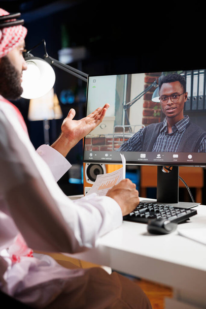 Видеозвонок заметно показан на экране компьютера, показывая разговор между мусульманским фрилансером и афроамериканским коллегой. Изображение подчеркивает использование современных технологий молодыми людьми. - Фото, изображение