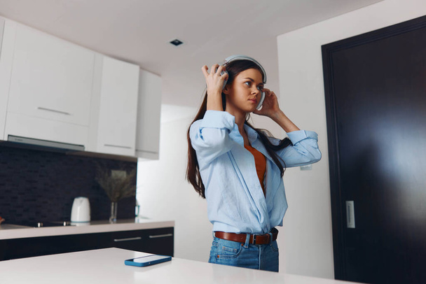 Наголошена жінка слухає музику перед кухонною стійкою з руками на голові в сучасній домашній обстановці - Фото, зображення