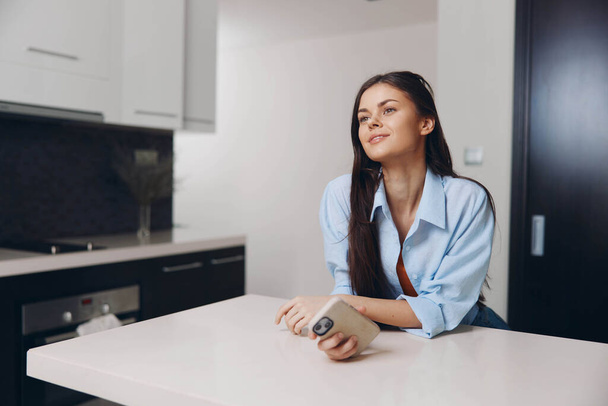 Жінка насолоджується чашкою кави в затишному кухонному середовищі, сидячи за столом з природним освітленням - Фото, зображення