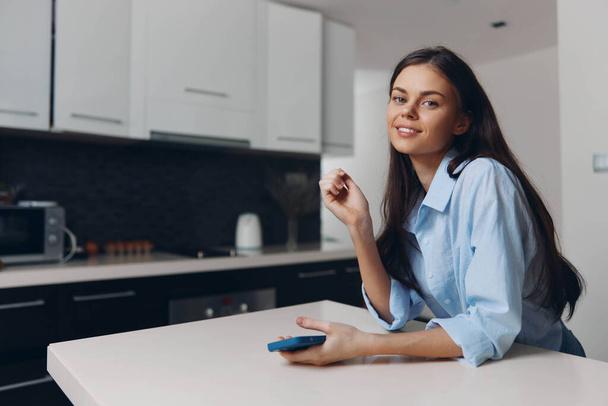 Жінка сидить за кухонним столом з пультом управління і чашкою кави в руці, насолоджуючись спокійним ранком вдома - Фото, зображення