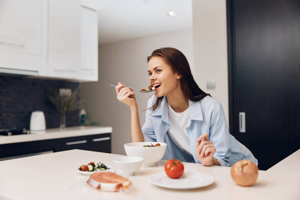 Жінка насолоджується їжею в затишному кухонному приміщенні, сидить за столом і їсть з миски - Фото, зображення
