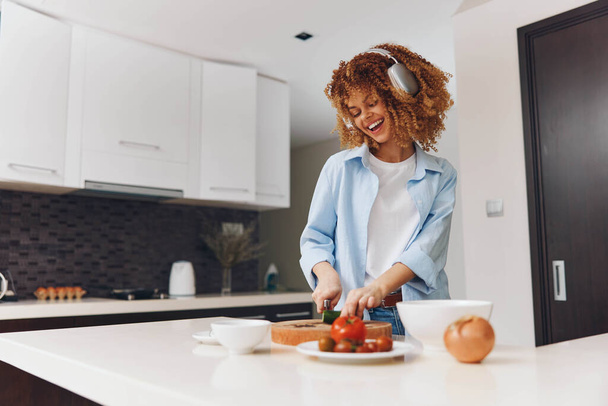 Feliz mujer afroamericana cocinando en su cocina casera con una sonrisa en la cara - Foto, Imagen