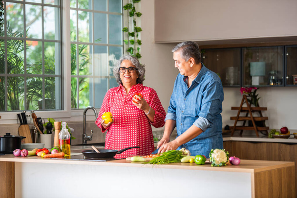 Senior Indian asian couple, cooking and having fun while preparing a healthy food in the kitchen at home - Photo, Image