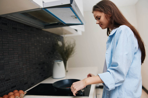 Nő kék ingben főzés tojás elektromos tűzhely a konyhában, kulináris koncepció - Fotó, kép
