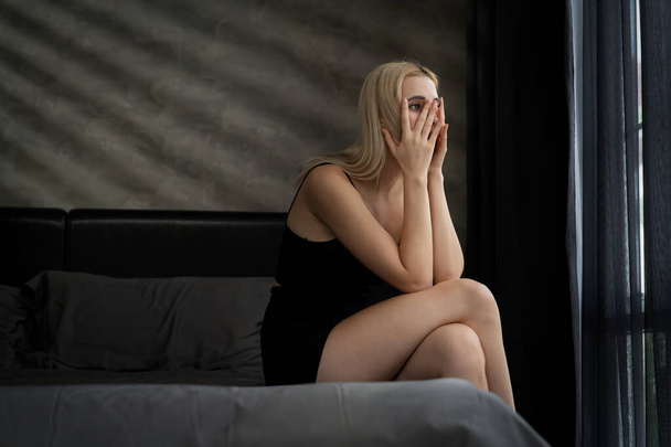 Молода жінка з критичною депресією і тривожним розладом від самотності, психічних захворювань або небажаної вагітності, присідає на темній спальні. Переважна негативна думка. Блайт - Фото, зображення