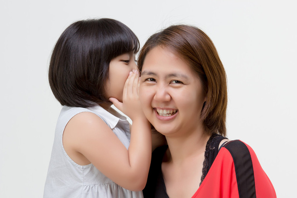 Retrato de madre asiática susurrando a su hija en aislado
 - Foto, Imagen