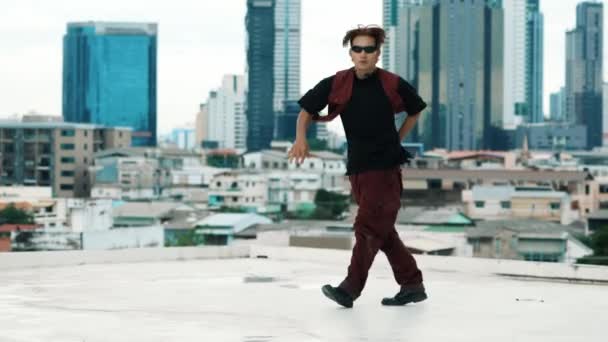 B-boy tánc előadás a profi utcai táncos a tetőn égi bunyós, városi kilátással. A vonzó ázsiai hipszter energikus lépteket mutat. Aktív break tánc. Szabadtéri sport 2024. hiphop. - Felvétel, videó