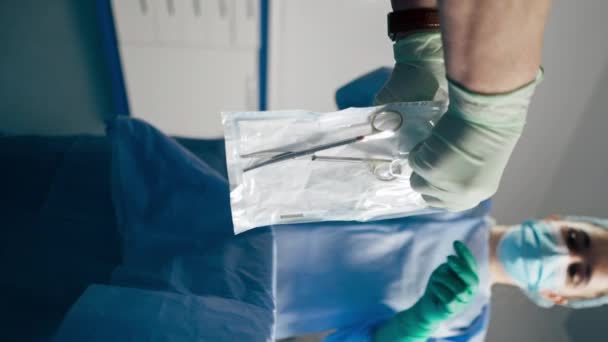 Vertikales Video im Operationssaal: Der untere Chirurg in grünen Handschuhen zieht eine Schere aus einer sterilen Verpackung - Filmmaterial, Video