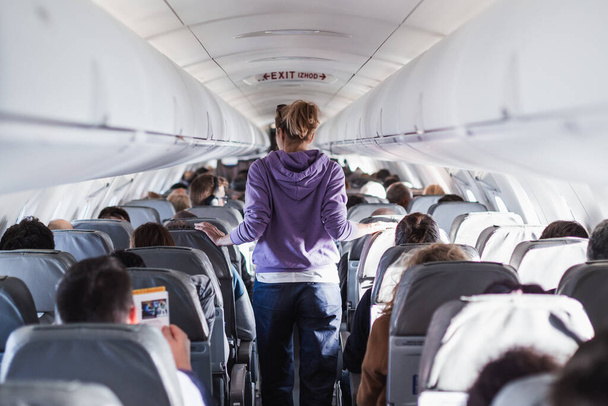 Sisätilojen lentokone matkustajien istuimet ja naispuolinen matkustaja kävelee käytävällä. Kaupallisen talouden lennonvarmistuspalvelujen käsite - Valokuva, kuva