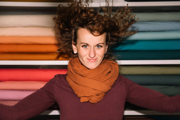 Радостная молодая женщина с кудрявыми волосами в магазине тканей - Фото, изображение