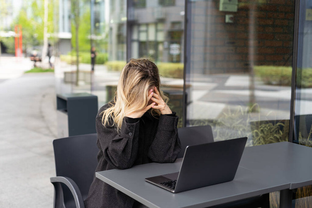 Moe jonge zakenvrouw in zwart pak met hoofdtelefoon zit met gesloten ogen voor laptop. Hoge kwaliteit foto - Foto, afbeelding