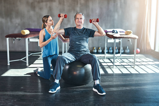 Fitness, personal trainer and senior man with dumbbell in gym for physiotherapy, support or workout. Recovery, female coach and elderly patient on ball for help, arthritis balance or rehabilitation. - Fotoğraf, Görsel