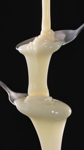 Molho de leite condensado doce branco que flui da colher de metal no fundo preto. Comida close up, câmera lenta, vídeo vertical 4K - Filmagem, Vídeo
