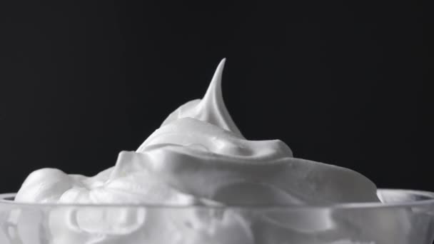 Chef takes whipped egg whites with sugar with a spoon from a glass bowl. Close-up of food on a black background, zoom in - Footage, Video
