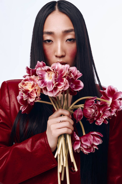 平和な屋外の設定でピンクの花束を保持する赤いジャケットの長い黒い髪の美しい女性 - 写真・画像