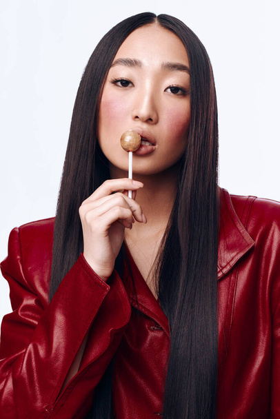 Retrato de joven mujer asiática con estilo con chaqueta de cuero rojo con piruleta en la boca - Foto, imagen