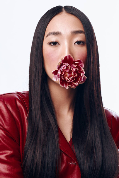 Mulher sedutora com cabelo preto longo em casaco vermelho segurando flor na boca, posando sedutoramente - Foto, Imagem