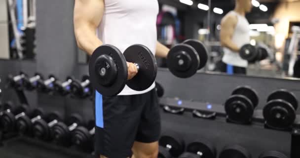 Starker Mann hebt schwere Hanteln, die in modernen Fitnessstudios stehen. Motivierter Sportler macht effektives Training mit Gewicht, um die Armmuskulatur in Zeitlupe hochzupumpen - Filmmaterial, Video