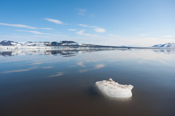 Una amplia vista de bajo ángulo del derretimiento de los témpanos de hielo marino en aguas tranquilas del Ártico Norte con montañas y tundra en el fondo.Crisis climática y colapso.Emergencia climática - Foto, Imagen