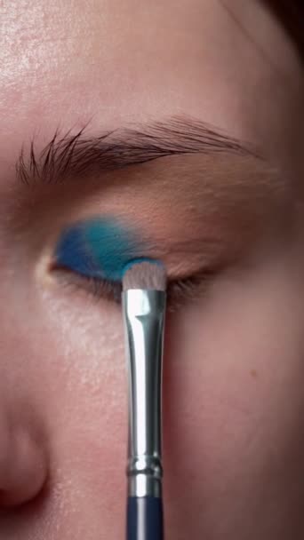 De make-up kunstenaar brengt vakkundig blauwe, diepe en aantrekkelijke schaduwen aan op de oogleden van het jonge model, waardoor de perfecte avondmake-up ontstaat. ectreme macro - Video